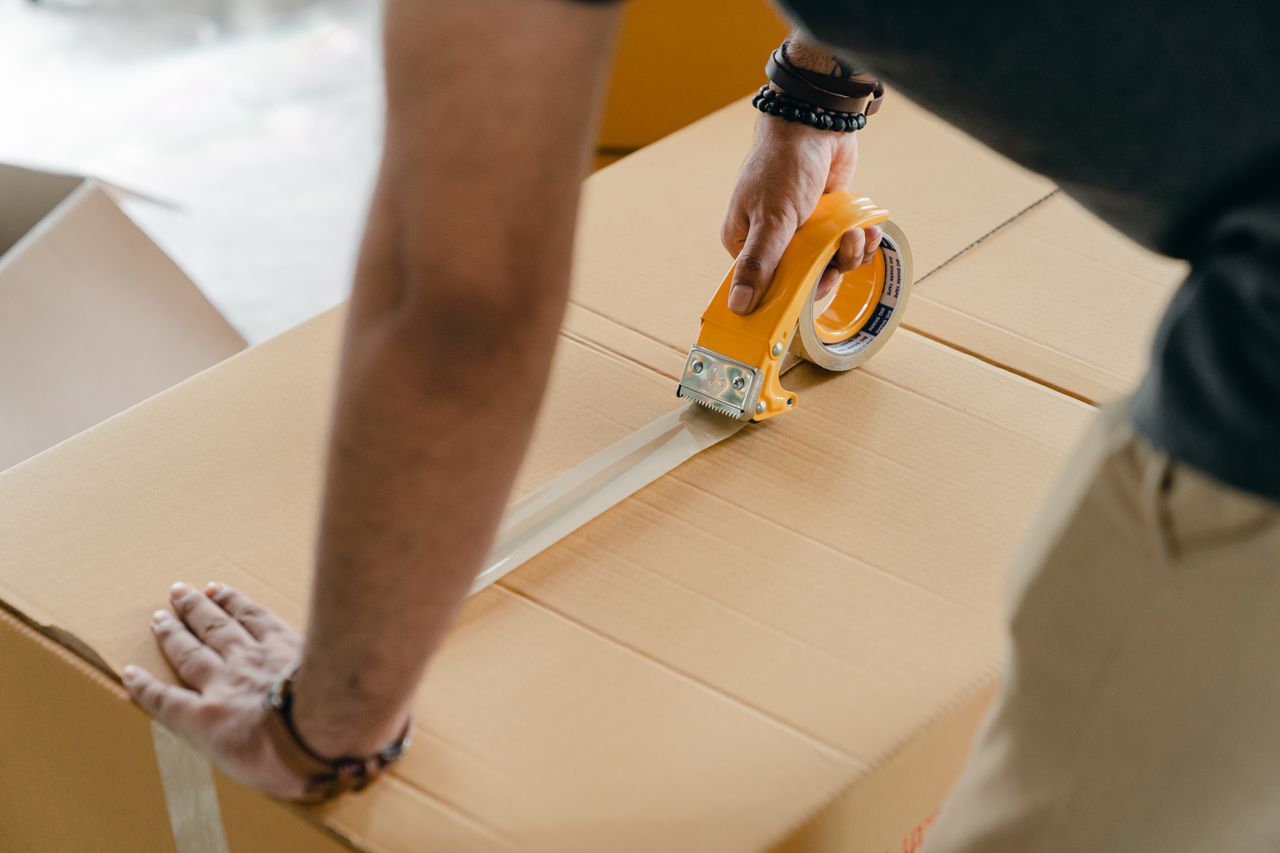 why-choose-us-01 From above of crop anonymous young male using adhesive tape while sealing cardboard box