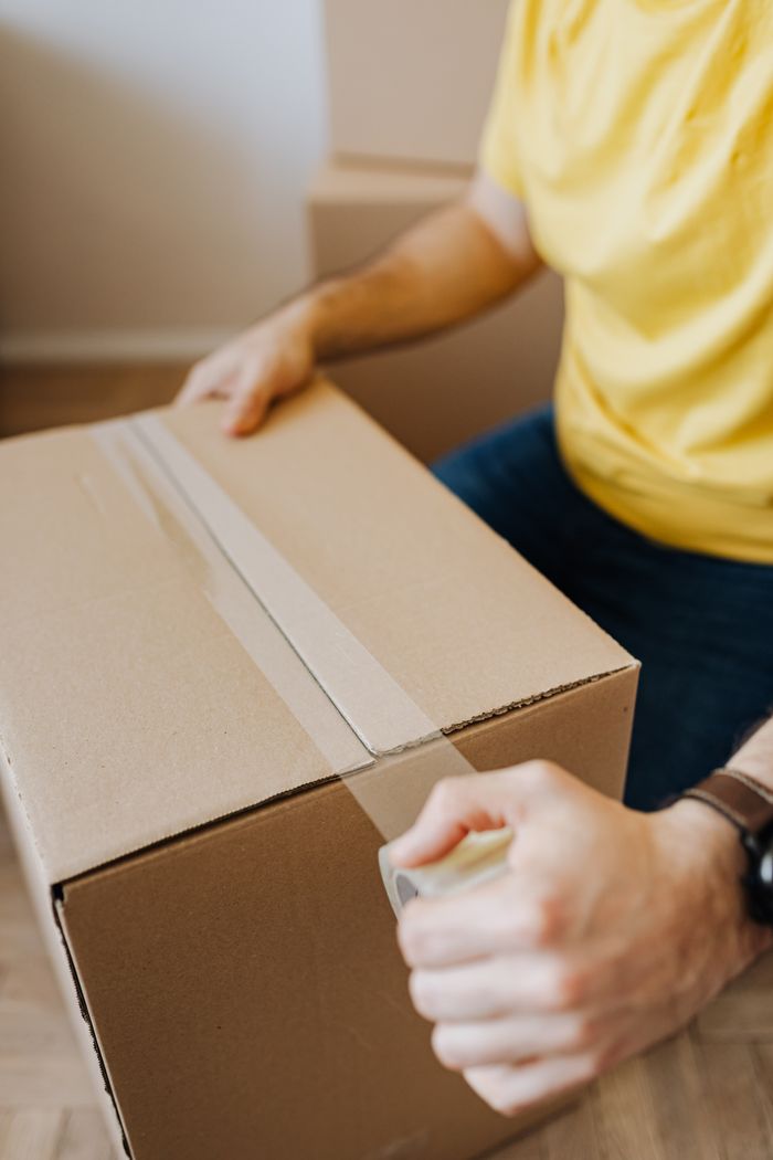 our-story-01 Crop anonymous guy in casual clothes using clingy tape to seal cardboard box for courier during relocation