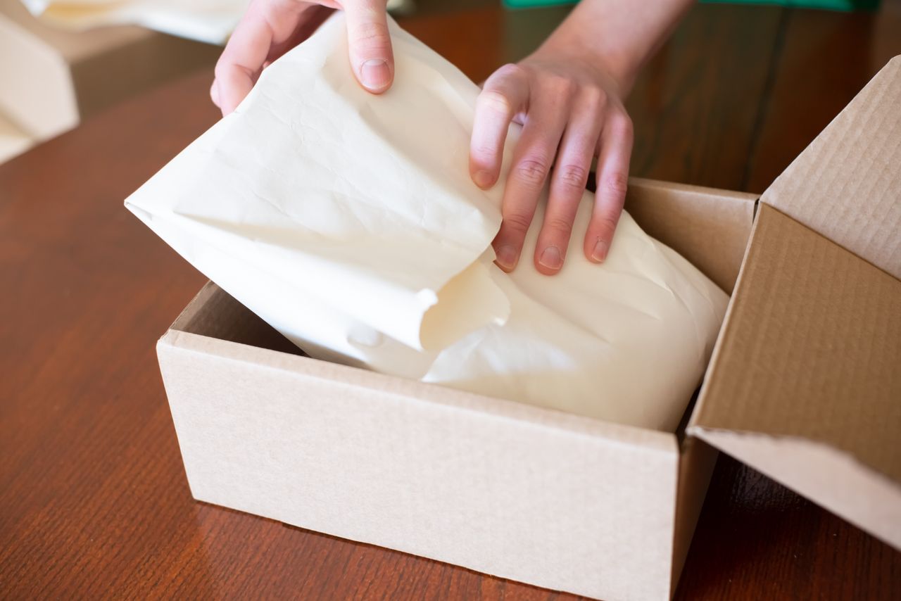 our-story-02 Hands wrapping merchandise in a cardboard box for shipping, ideal for small business stock images.